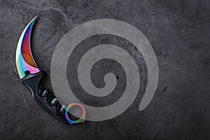 Kerambit dagger with a rainbow-colored blade on a dark textured background.