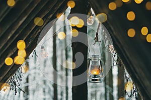 Kerosene lamp with garland hanging on bushcraft survival shelter under roof in winter forest
