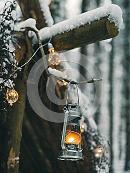 Kerosene lamp and garlands hanging on survival shelter in winter forest