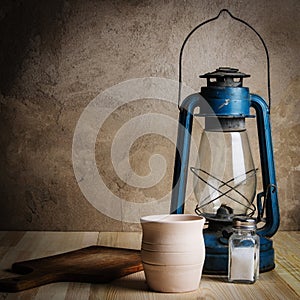 Kerosene lantern, cutting board and clay pot on a wooden table