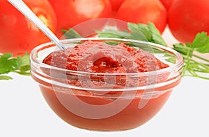 Ketchup in glass dish on background of red tomatos