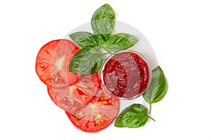 Ketchup tomato paste in a saucepan with basil leaves and tomato slices on a white background.