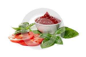 Ketchup tomato paste in a saucepan with basil leaves and tomato slices on a white background