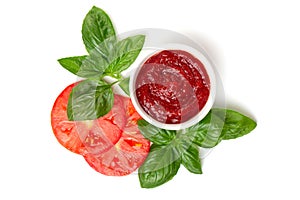 Ketchup tomato paste in a saucepan with basil leaves and tomato slices on a white background