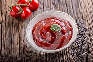 Ketchup or tomato sauce in white bowl and cherry tomatoes on wooden table