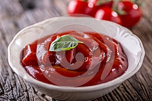 Ketchup or tomato sauce in white bowl and cherry tomatoes on wooden table