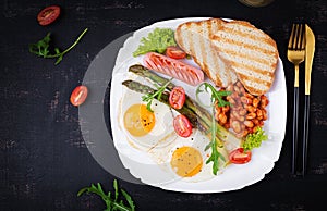 Keto breakfast. Breakfast. Fried eggs, bread toast, green asparagus, beans and sausage on white plate. Top view, flat lay