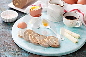 Keto carnivore diet breakfast. Soft-boiled eggs, liver roll pate with butter, goat cheese and coffee on a wooden plate