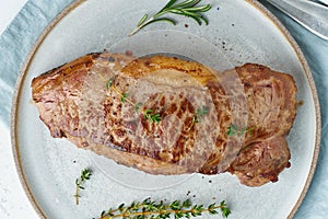 Keto ketogenic diet beef steak, striploin on gray plate on white background. Paleo food recipe with whole big piece of meat and