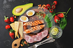 Keto, ketogenic diet, low carbohydrate content. Grilled salmon, vegetables, strawberries, cheese, ham and water with lemon. Black