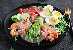 Ketogenic diet breakfast. Salt salmon salad with boiled shrimps, prawns, tomatoes, spinach, eggs and avocado.