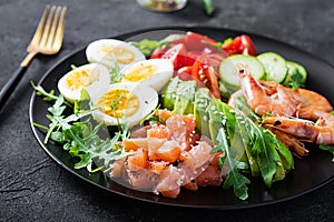 Ketogenic diet breakfast. Salt salmon salad with boiled shrimps, prawns, tomatoes, spinach, eggs and avocado.