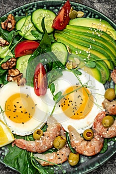 Ketogenic diet breakfast shrimps, prawns, soft fried egg, fresh salad, tomatoes, cucumbers and avocado on a dark background. Keto