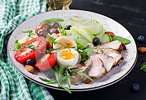 Ketogenic diet. Boiled egg, pork steak and olives, cucumber, spinach, brie cheese, nuts and tomato