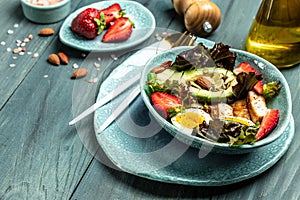 Ketogenic low carbs diet, Plate with keto foods: two eggs, avocado, grilled chicken fillet, nuts, strawberries and fresh salad.