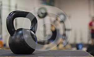 A cast iron kettle bell with a young women weight lifting in the background