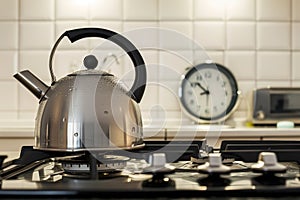 kettle with boiling water on a ceramic hob, kitchen clock in background