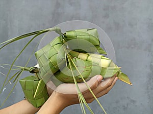 Ketupat (Rice Dumpling) in hands on gray wall background. Ketupat is natural rice casing made from young coconut leaves