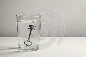 A key in a glass of water on a light background. Space for text.