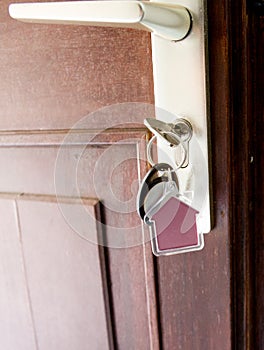 Key on house shaped keyring in lock of entrance brown door