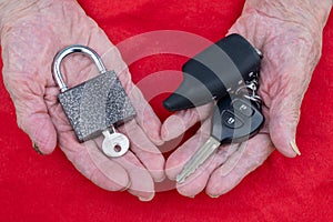 Key and lock, car key in the hands of an old woman on a red background. The concept of new technologies