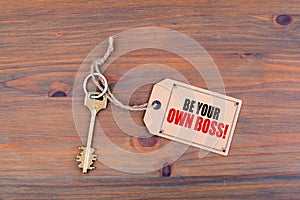 Key and a note on a wooden table with text - Be Your Own Boss photo