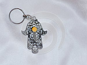 A key ring in the form of Fatima Hand on a white silk background. Ancient symbol and traditional modern tourist souvenir of