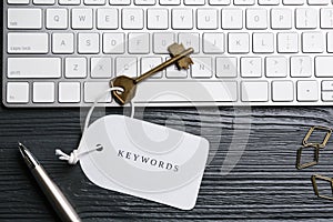 Key with tag KEYWORD and computer keyboard on black wooden table, flat lay