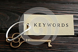 Key with tag KEYWORDS on wooden background, closeup