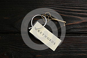 Key with tag KEYWORDS on wooden background, top view