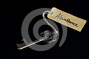 Key to abundant life concept - Old key with abundance tag isolated on black background