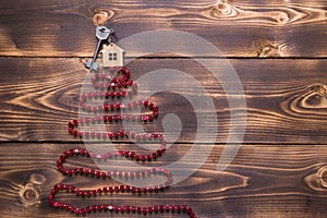 Key to the house with a keychain on top of Christmas tree made of red square beads. Flat lay on wooden background. Building or