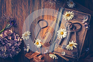 Key to knowledge concept. Old keys on a vintage book with flowers on wooden background