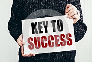 KEY TO SUCCESS text on white card in the hands of a man in black sweater on white background