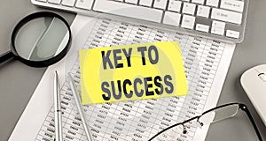 KEY TO SUCCESS text written on a sticky on chart with keyboard and magnifier