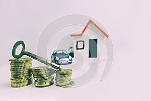 Key on top of a stack of coins with a blurred house and car on the background: real estate, property, mortgage, concept