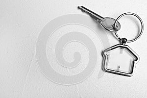 Key with trinket in shape of house on stone background, top view and space for text. Real estate agent services