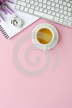 Keyboard, alarm clock and cup of tea on a pink feminine table. Vertical minimal flat lay with copy space