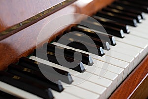 The keyboard of a brown upright piano on a blurred background.