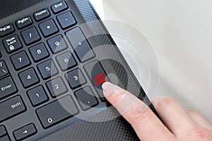 Keyboard corner of a black laptop with a female finger clicking on a fake news button. The concept of spreading false news