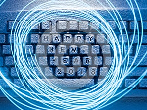 Keyboard covered with snow illuminated by light with circles painted by light with the inscription happy new year 2018