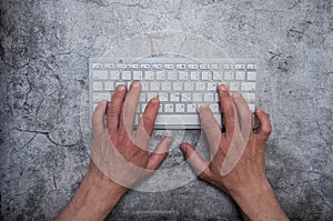 Keyboard with hands on a dark gray background. Asphalt concrete wallpaper. Context, writer, programmer, office work.