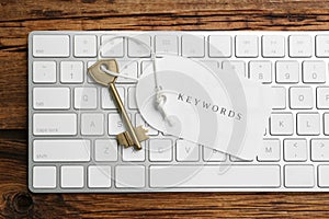 Keyboard, key and tag with word KEYWORDS on wooden table, top view
