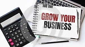 Keyboard of laptop, calcualtor, pencil and notepad with text GROW YOUR BUSINESS on the white background