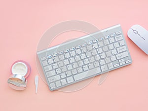 Keyboard and mouse near a face cream container on pink