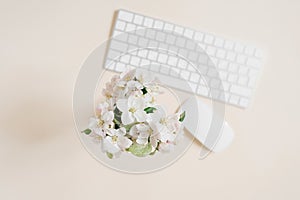 Keyboard and mouse and white apple flowers in a vase out of focus on a beige table. Layout and design concept. Flat lay