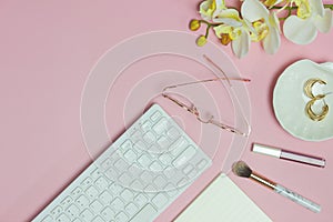 Keyboard, notebook, glasses and flowers over the pink background.