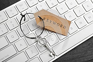 Keyboard, vintage key and tag with word KEYWORD on black table, closeup