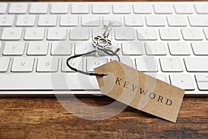 Keyboard, vintage key and tag with word KEYWORD on wooden table, closeup