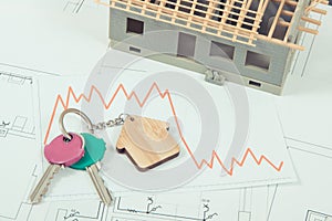 Keys and downward graphs representing crisis of real estate market. Reduced housing prices. House under construction